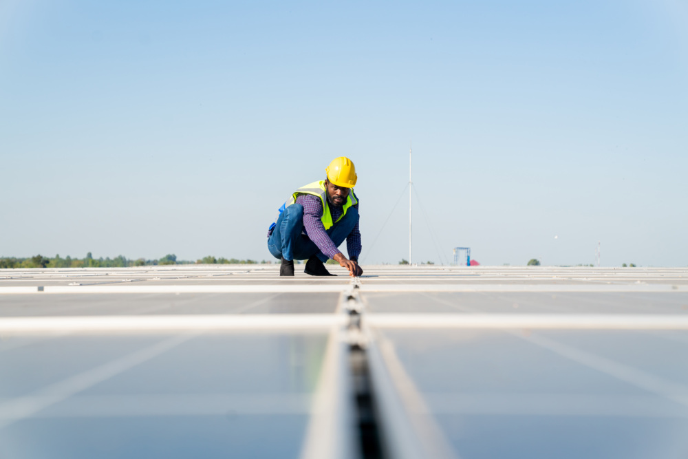 A person in a yellow hard hat and blue vest inspects solar panels under the bright Massachusetts sun, showcasing how climate-conscious careers are vital for our sustainable future.